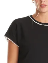 Blusa de crepe color blanco, con cuello redondo y mangas cortas. Presenta apliques de perlas decorativas en el borde del cuello y en los extremos de las mangas.