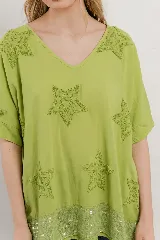 Blusa lila de algodón con escote en V, mangas cortas y holgadas. Presenta estrellas bordadas en relieve en la parte superior y un borde de lentejuelas en el dobladillo inferior.