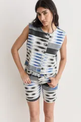 Chaleco de denim con estampado abstracto en tonos azul, gris y negro, con cierre frontal de botones y ruedo desflecado.