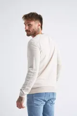 Sweater de tejido de punto color beige, con escote en V, mangas largas y puños y dobladillo acanalados. Presenta un pequeño logo bordado en el pecho.