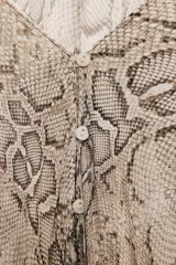 Blusa de escote en V con estampado de piel de serpiente en tonos beige y marrón. Tiene mangas largas tipo murciélago con puños ajustados y cierre frontal con botones.