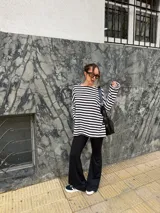 Conjunto compuesto por remera de manga larga oversize a rayas horizontales blancas y negras con escote bote, y pantalón negro de corte flared.