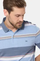 Remera polo de manga corta con cuello y puños en azul oscuro. Presenta un diseño de rayas horizontales en tonos de azul claro, azul oscuro, blanco, amarillo, rosa y verde. Incluye botones personalizados y un logo bordado en el pecho.
