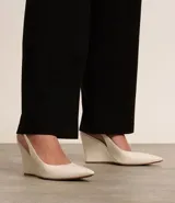 Zapato de tacón tipo anabela (cuña) color marrón oscuro, con punta fina y diseño slingback con tira elástica en el talón. Confeccionado en poliuretano con acabado liso.