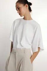Camiseta blanca de manga corta con corte oversize y cuello redondo. El diseño presenta mangas amplias tipo capa que caen desde el hombro.