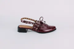 Sueco de cuero color borgoña con cordones, ojales y hebillas plateadas. Tiene tira trasera regulable con elástico.