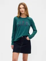 Remera de manga larga color verde oscuro, con cuello redondo y logo de la marca Gap estampado en el frente con diseño de cuadros escoceses.