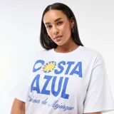 Remera blanca de corte oversize y manga corta, con estampa frontal en tonos azules y amarillos que incluye el texto 'Costa Azul' y 'Palma de Mallorca'.