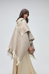 Ruana de lana sin teñir en tono marrón jaspeado, con diseño envolvente y terminaciones de flecos en color crudo.