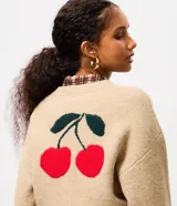 Cardigan de punto color beige con cierre frontal, cuello redondo, mangas largas y detalle bordado de cerezas en el pecho. Presenta puños y ruedo acanalados.