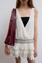 Vestido corto de gasa color blanco, con escote en V cruzado, sin mangas y diseño con volantes en el bajo. Presenta un detalle de tachas plateadas en la cintura.