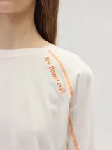 Remera manga larga de algodón color crudo, con cuello redondo y calce holgado. Posee costuras a la vista en color naranja y un delicado bordado con la frase "the flower edit" sobre el hombro izquierdo.