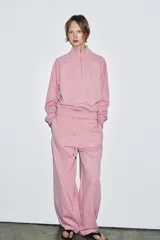 Sudadera de algodón color rosado con cuello alto, cierre frontal con cremallera metálica y manga larga. Presenta aplicación metálica en el pecho y acabados en rib.