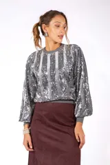 Sweater de cuello redondo y mangas largas abullonadas, confeccionado con un diseño de rayas verticales alternadas entre tejido liso y lentejuelas brillantes.