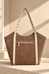 Cartera tipo tote de gamuza color azul marino, con asas dobles de cuero marrón texturado y detalles de tachas metálicas plateadas. Cuenta con una placa metálica frontal con el logo de la marca Pecarí.