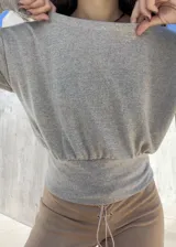 Buzo de tela angorina elastizada color gris, con diseño de cuello bote que permite usarlo con un hombro descubierto. Presenta un corte amplio en la parte superior y una cintura ajustada, con mangas largas.