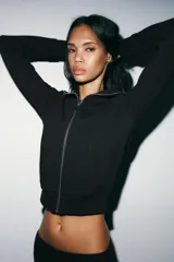 Chaqueta de felpa color gris claro melange, con cuello solapa, manga larga con puños elastizados, bolsillos frontales y cierre de cremallera completa.