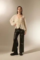 Blusa de poliéster color natural, con cuello en V, mangas largas con puños elásticos y detalle de frunces con cordón ajustable en el frente.