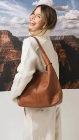 Cartera tipo hobo de cuero texturizado, color marrón, con diseño amplio y correa de hombro integrada.
