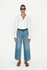 Jeans de tiro alto con pernera ancha y corte cropped. Presenta diseño de cinco bolsillos, cierre frontal con cremallera y botón, e incluye un cinturón oscuro con hebilla metálica.