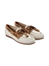 Mocasín de cuero estilo náutico, en combinación de color crema y marrón gamuzado. Presenta detalles de costuras artesanales, cordones de cuero cruzados con ojales metálicos, flecos y borlas decorativas en el empeine.