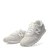 Championes urbanos New Balance modelo 373, color gris claro con detalles en beige y blanco. Confeccionados en una combinación de gamuza y malla, presentan el logo "N" característico en los laterales y una suela de goma con entresuela amortiguada.