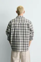 Camisa de corte boxy fit confeccionada en tejido de algodón con elasticidad. Presenta un diseño a cuadros, cuello solapa, manga larga con puños abotonados, bolsillo de vivo en el pecho y cierre frontal con botones.