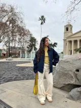 Cartera tipo hobo de cuero gamuzado color verde oliva, con cierre superior y correa ajustable. Presenta una etiqueta de cuero con el logo de la marca en el frente.