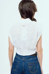 Top blanco sin mangas de broderie, con cuello alto, hombreras y cierre frontal de botones.