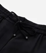 Pantalón de corte fluido y estilo pijama, color negro, con cintura elástica ajustable mediante lazo y detalle de tiras con hebilla en los tobillos.