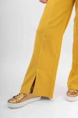 Pantalón ancho de color mostaza con costuras contrastantes en blanco. Presenta un corte recto y aberturas en los bajos delanteros.