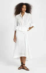 Camisa de rayas verticales blanca de Le Lis Blanc, modelo Regina, confeccionada en tejido fluido con ligera transparencia. Presenta corte recto, cuello clásico, mangas largas con volumen y puños ajustados, cierre frontal de botones y detalle fruncido con cordón en la cintura.