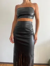 Falda midi negra de cuero sintético, corte ajustado y flecos largos en el ruedo.