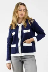 Chaqueta azul marino tejida en lana con ribetes blancos, cuello redondo, cierre frontal con botones dorados y bolsillos frontales con solapa blanca.