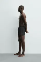 Short de baño negro de tejido técnico con estructura ripstop resistente a desgarros, cintura ajustable con cordón y bolsillos laterales.