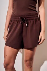 Short marrón de corte holgado, con cintura elástica fruncida y cordón ajustable con punteras metálicas.