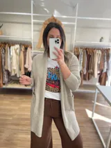 Saco largo color crema, de tejido de punto, con bolsillos laterales y corte recto.