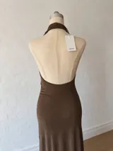 Vestido midi de color marrón, con escote halter profundo y diseño drapeado en la parte frontal. Presenta un tajo lateral con cordón ajustable y espalda descubierta.