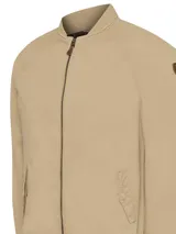 Campera bomber color beige de sarga de algodón orgánico con calce regular. Tiene cierre frontal, dos bolsillos delanteros con tapeta y snaps ocultos, dos bolsillos internos, puños, cuello y pretina de rib. El interior está forrado con franela.