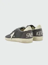 Zapatillas Golden Goose modelo Ballstar Nabuk, confeccionadas en gamuza y cuero color gris oscuro, con la característica estrella blanca en el lateral, suela con efecto desgastado y detalles de inscripción dorada.