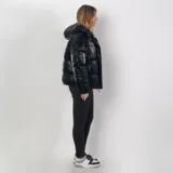 Campera puffer negra de poliéster con interior acolchado, capucha ajustable, cuello alto, cierre frontal con cremallera y botones a presión, dos bolsillos externos con cierre y sistema de ajuste regulable en la parte baja.