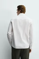 Camisa de corte regular fit color blanco, confeccionada en tejido de algodón con efecto arrugado, con cuello solapa, manga larga, puños abotonados y un bolsillo de parche en el pecho.