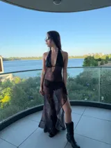 Vestido largo de estilo etéreo y fluido, confeccionado en tela semitransparente con estampado tipo tie-dye en tonos oscuros. Presenta un escote profundo tipo halter con tiras que se anudan al cuello y una falda con tajo lateral que aporta movimiento.