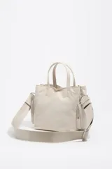 Bolso tipo tote y bandolera de color beige, con bolsillos externos con cierre y asas de mano y hombro.