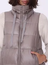 Campera larga sin mangas color visón, con cuello alto y cierre frontal.