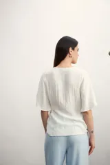 Camisa negra con botones dorados, escote en V y mangas cortas amplias con lazos laterales. 