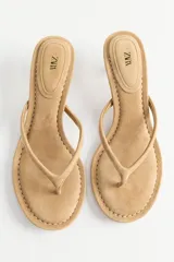 Sandalia de tacón kitten de serraje color beige, con tira tipo chinela que incluye una posición para el dedo. Presenta pespunte en contraste y punta redonda.