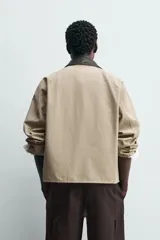 Sobrecamisa de corte relajado color beige, con cuello solapa en efecto piel de color negro. Presenta cierre frontal con cremallera, bolsillos de vivo en la cadera y mangas largas con puños ajustables.