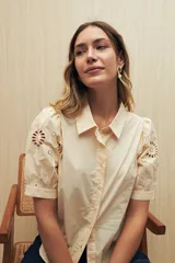 Camisa color crema o amarillo muy pálido, con cuello clásico y mangas cortas abullonadas que presentan bordados calados florales (broderie anglaise).