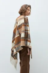 Ruana de tejido grueso con diseño de cuadros en tonos beige, marrón y gris, con terminación de flecos en los bordes.